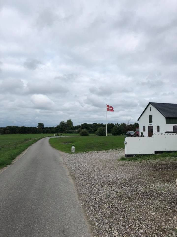 Lundholm Festlokale set udefra med dannebrog og de åbne marker ved Arresø i Skævinge